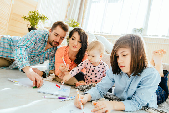 Young happy family of four drawing together while lying on floor at home. New home, happy healthy relationship concept.