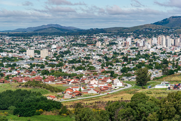 Fototapeta premium View from a mountain of a grove, the city of Tandil and a mountain range on the back with a few clouds on the sky