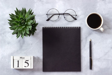 Office or home table desk. Wooden cubes calendar May 15. Black notepad, cup of coffee, succulent, glasses on marble background Concept stylish workplace Flat lay Top view