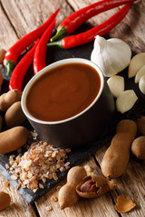 Homemade tamarind sauce surrounded by ingredients close-up in a bowl on table. vertical