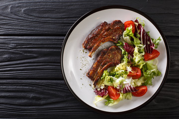 Delicious fried lamb chops served with fresh vegetable salad close-up on a plate. Horizontal top...
