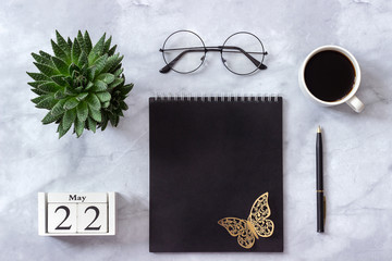 Office or home table desk. Wooden cubes calendar May 22. Black notepad, cup of coffee, succulent, glasses on marble background Concept stylish workplace Flat lay Top view