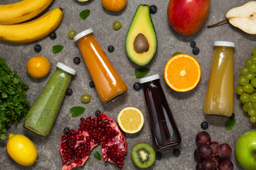 Colorful smoothies in bottles with fresh tropical fruit and vegetables on concrete background, top view. Flat lay.  Healthy, clean eating, vegan, vegetarian, detox, dieting food concept.