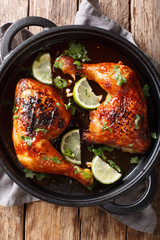 Spicy fried tamarind chicken quarter leg with lime close-up in a frying pan. Vertical top view