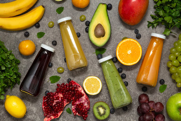 Colorful smoothies in bottles with fresh tropical fruit and vegetables on concrete background, top view. Flat lay.  Healthy, clean eating, vegan, vegetarian, detox, dieting food concept.