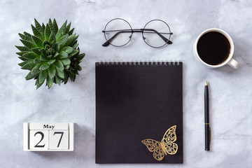 Office or home table desk. Wooden cubes calendar May 27. Black notepad, cup of coffee, succulent, glasses on marble background Concept stylish workplace Flat lay Top view