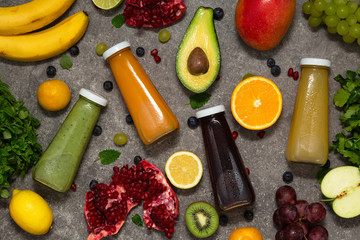Colorful smoothies in bottles with fresh tropical fruit and vegetables on concrete background, top view. Flat lay.  Healthy, clean eating, vegan, vegetarian, detox, dieting food concept.