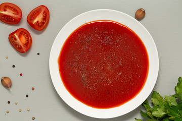 Tomato soup in a white bowl on grey background. Delicious soup of tomatoes and fresh herbs with garlic and spices. Top view.
