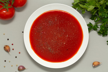 Tomato soup in a white bowl on grey background. Delicious soup of tomatoes and fresh herbs with garlic and spices. Top view.