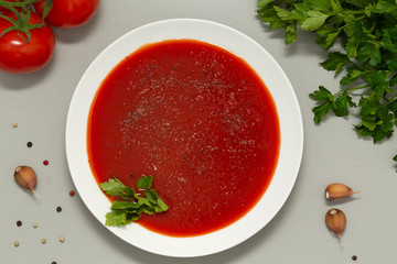 Tomato soup in a white bowl on grey background. Delicious soup of tomatoes and fresh herbs with garlic and spices. Top view.