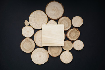 Pine tree cross-sections with annual rings and wooden square onblack surface. Lumber piece close-up shot, top view.