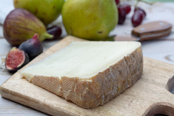 Piece of French cheese Tomme de Brebis made from sheep milk served as dessert with fresh figs and pears