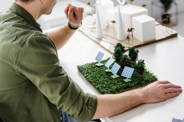 cropped view of architect sitting at table with solar panels and trees models in office