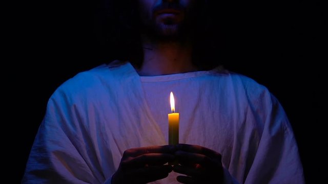 Parishioner in robe with burning candle, praying God in darkness, Christianity