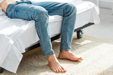 cropped view of man in jeans lying on bed in bedroom