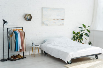 bed, clothes rack with shirts, plant, floor lamp and coffee table in bedroom
