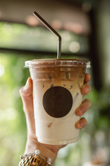 Woman hand holding a glass of coffee late with empty black circle logo in coffee shop.