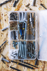 Plastic transparent organizer with screws, dowels, drills, bits on the background of the OSB.