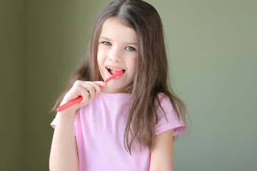 Girl brushing her teeth. Long haired smiling beautiful caucasian white girl brushing teeth with pink toothbrush on green background. Green eyed cute child in pink tshirt doing her morning hygiene. 