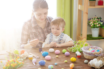 Mother and her son painting colorful Easter eggs. Happy family Mom and children son paint easter eggs with colors. Preparation for holiday.