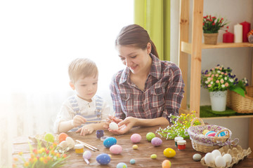 Mother and son painting Easter eggs. Happy family Mom and children son paint easter eggs with colors. Preparation for holiday.