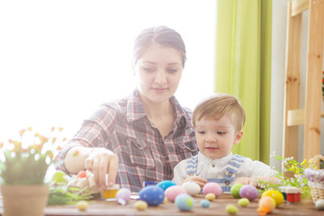 Easter concept. Happy mother and her cute child getting ready for Easter by painting the eggs. Happy family Mom and children son paint easter eggs with colors. Preparation for holiday.