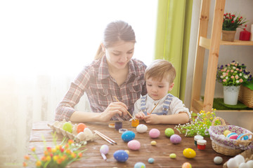 Happy family Mom and children son paint easter eggs with colors. Preparation for holiday.