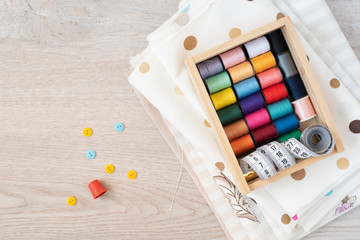 Composition with sewing threads, fabrics and accessories on wooden background, top view