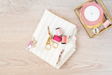 Composition with matte pink colors sewing threads and accessories on wooden background, top view