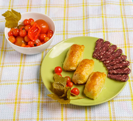 Pastries, smoked sausage and cherry tomatoes on a plate.