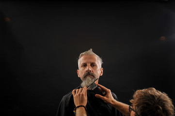 barber cuts a beard to a client to an elderly gray-haired man