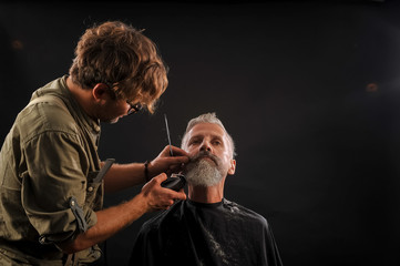 barber cuts a beard to a client to an elderly gray-haired man