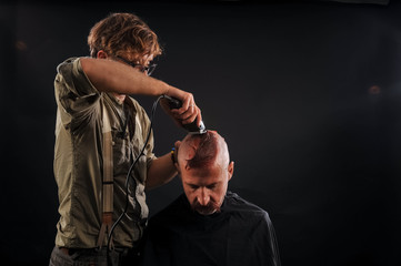 the barber shaves his head bald elderly man in the studio