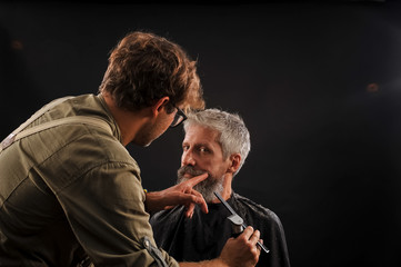 barber cuts a beard to a client to an elderly gray-haired man