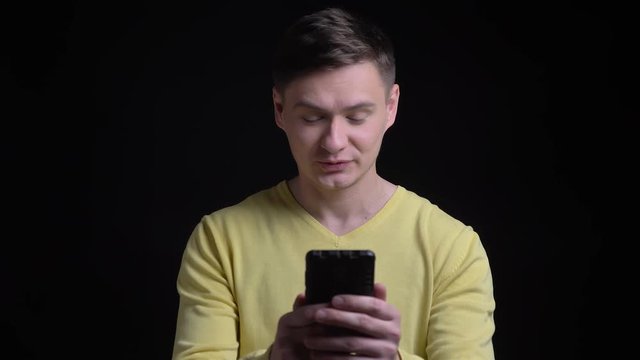 Portrait of smiling middle-aged caucasian man in yellow sweater talking in videochat happily on smartphone on black background.