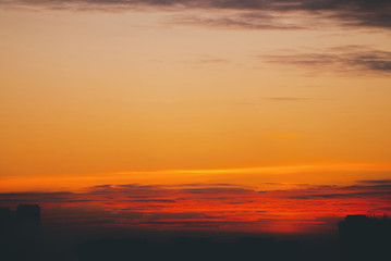 Cityscape with vivid fiery dawn. Amazing warm dramatic cloudy sky above dark silhouettes of city...