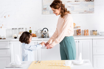 Mother and little daughter folding napkins while standing in kitchen