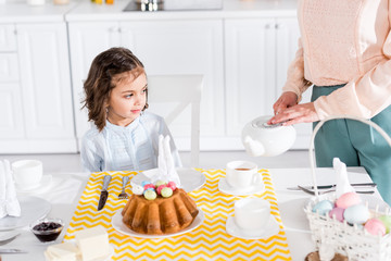 Cropped view of woman with teapot pouring tea for daughter