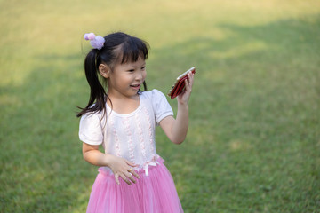 children thai girl standing are watching cartoon movies on smartphone with high-speed 4G WI-FI system in the garden Greenland