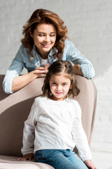 Fototapeta na wymiar Smiling mother and daughter sitting on sofa and using smartphone