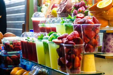 Shelves with aligned plastic glasses of different types of fresh fruit juice and fresh strawberries , sliced oranges and pomegranates