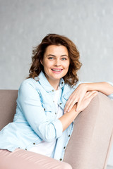 Inspired brunette woman in shirt sitting on sofa with closed eyes on grey