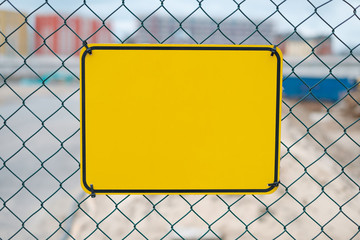 blank yellow sign on construction site fence - warning sign mockup,
