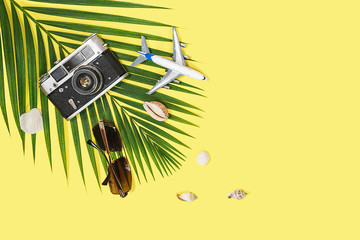 Flat lay with traveler accessories: tropical palm leaf, retro camera, model airplane, fashion sunglasses and seashells on yellow background, with space for text. Travel, summer concept. Top view.