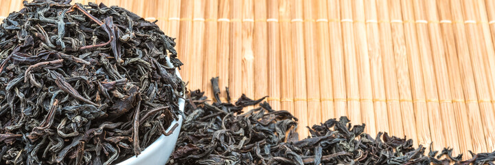 Dried tea is poured into a ceramic cup on a bamboo mat.