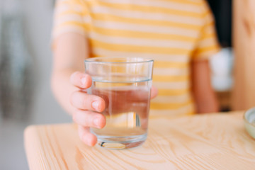The glass of clean water in child hand, close up and selective focus