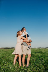 Happy family: young father, mother and his little son walking and hugging in field at summer day