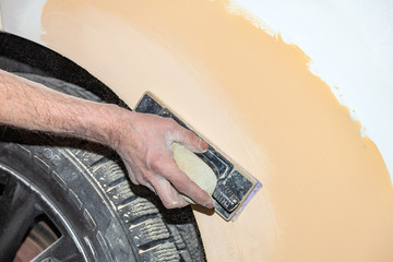 Preparation for painting a car element using emery sender by a service technician leveling out...
