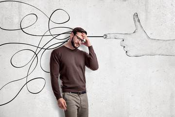 Thinking young man in casual clothes with a hand shooting gesture and abstract lines drawn on white wall background