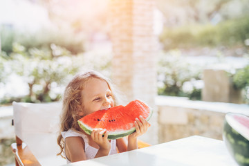 little preschool girl tasting ripe watermelon sitting in a patio surrounded by olive trees